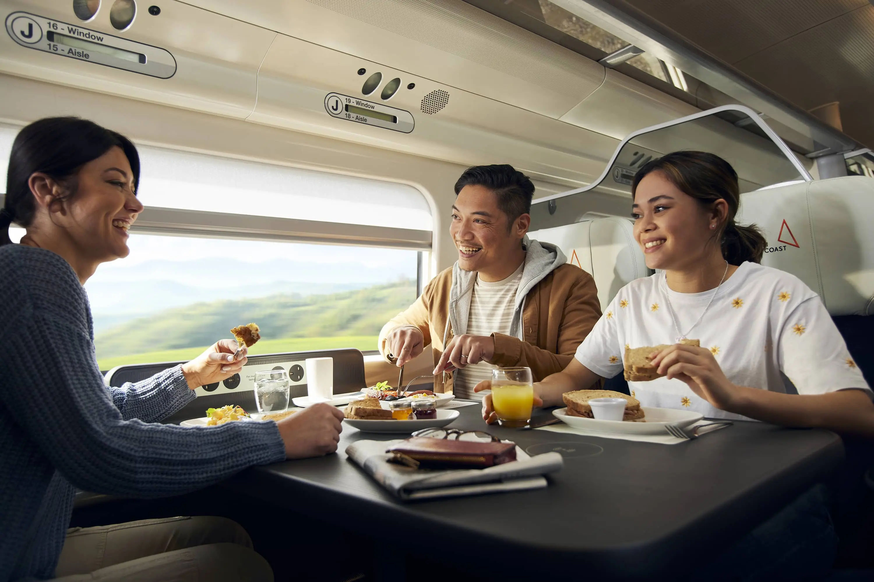 Three people in First Class sat at a table eating breakfast.